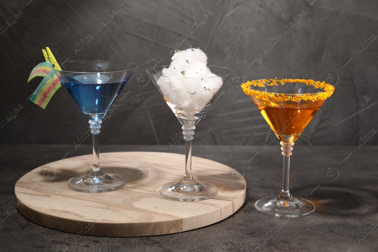 Photo of Tasty cotton candy cocktail and other alcoholic drinks in glasses on gray textured table