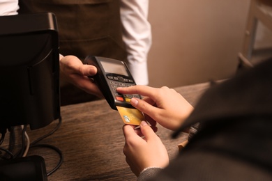 Photo of Woman with credit card using payment terminal at shop, closeup