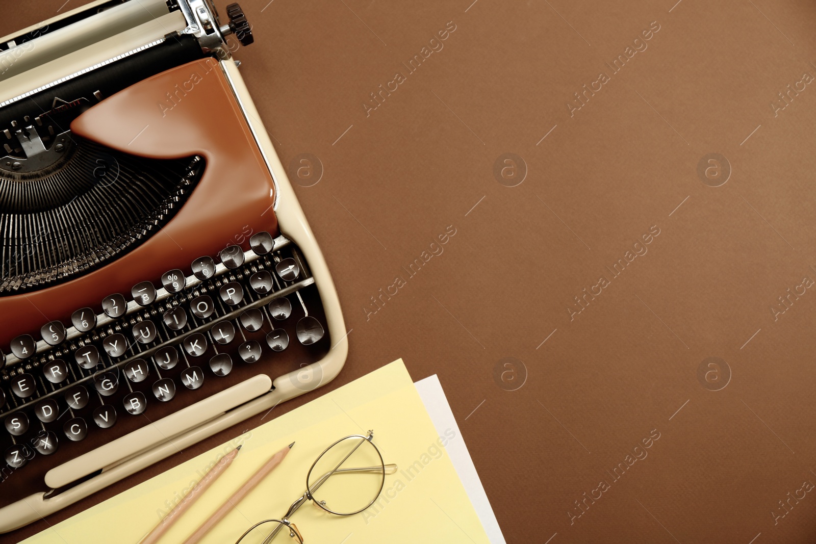Photo of Vintage typewriter, glasses and stationery on brown background, flat lay. Space for text