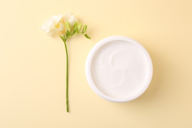 Photo of Moisturizing cream in open jar and freesia flower on beige background, flat lay. Body care product