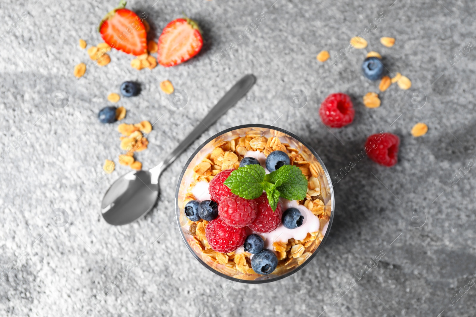 Photo of Glass of tasty homemade granola dessert on grey table, flat lay. Healthy breakfast