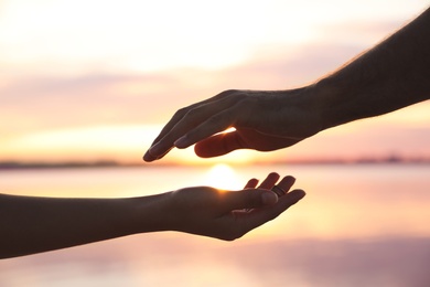 Photo of Man and woman reaching hands to each other at sunset, closeup. Nature healing power