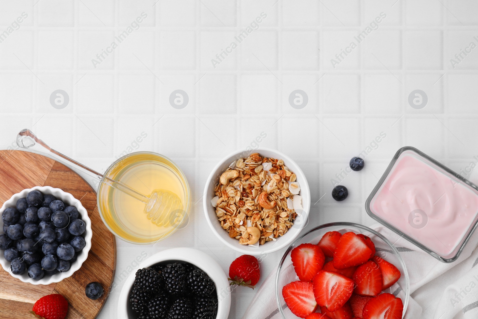 Photo of Tasty oatmeal, fresh berries, yogurt and honey on white tiled table, flat lay with space for text. Healthy breakfast