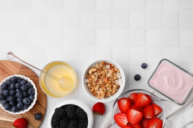 Photo of Tasty oatmeal, fresh berries, yogurt and honey on white tiled table, flat lay with space for text. Healthy breakfast