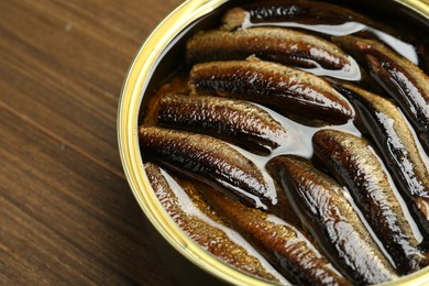 Sprats in tin can on wooden table, closeup. Space for text