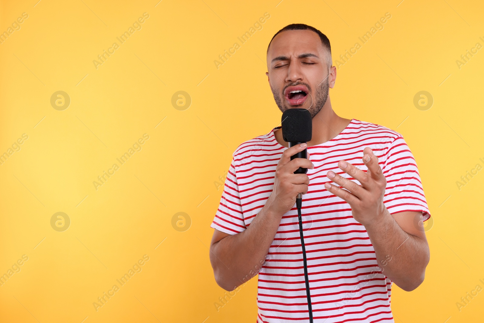 Photo of Handsome man with microphone singing on orange background. Space for text