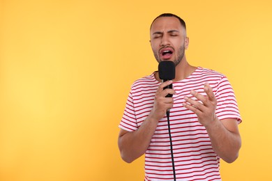 Handsome man with microphone singing on orange background. Space for text