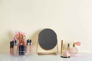 Photo of Mirror and makeup products on white table near light wall