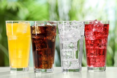 Photo of Glasses of different refreshing soda water with ice cubes on white table outdoors