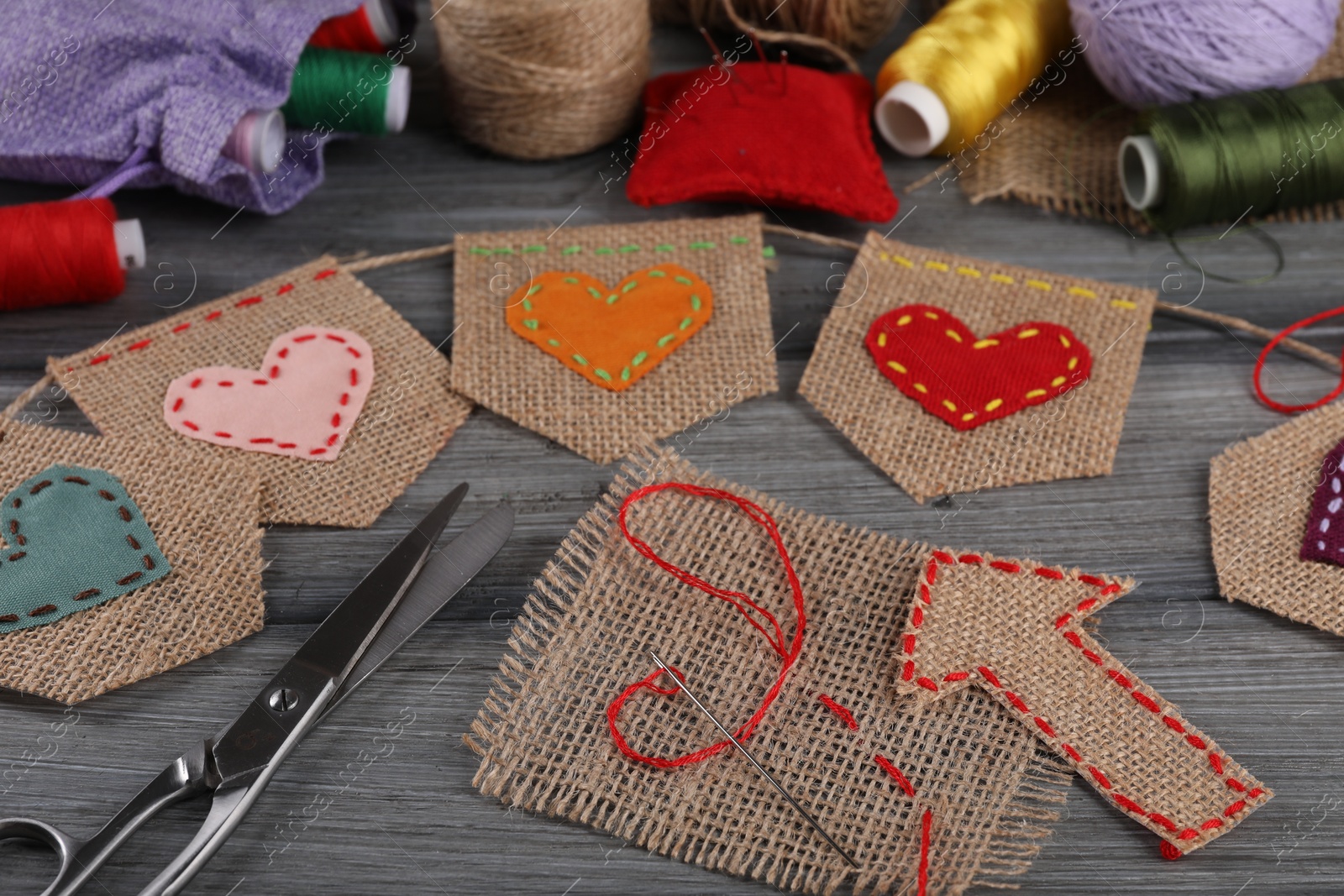 Photo of Bunting flags made with burlap fabric and sewing tools on wooden table, closeup
