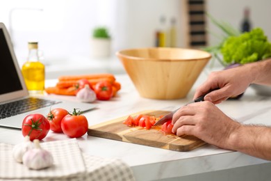 Man making dinner while watching online cooking course via laptop in kitchen, closeup