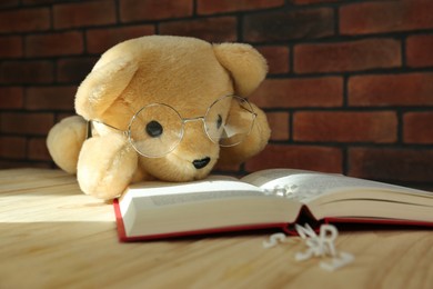 Photo of Dyslexia. Teddy bear with open book and letters on wooden table, closeup