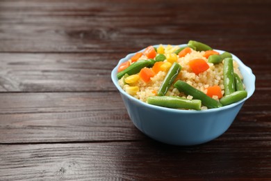 Photo of Delicious bulgur with vegetables in bowl on wooden table, closeup. Space for text