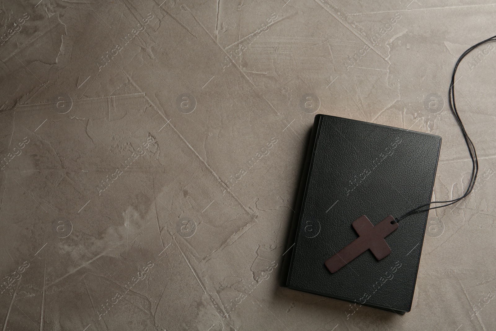 Photo of Wooden Christian cross and Bible on grey table, top view. Space for text