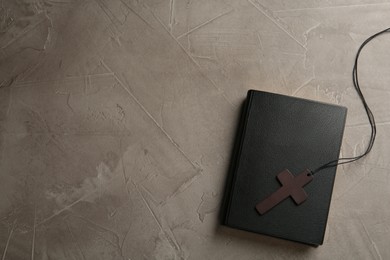 Wooden Christian cross and Bible on grey table, top view. Space for text