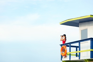 Photo of Female lifeguard with binocular on watch tower against blue sky