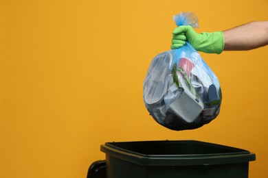 Photo of Man throwing garbage bag into bin on yellow background, closeup. Space for text