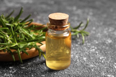 Bottle with oil and fresh rosemary on grey textured table, closeup