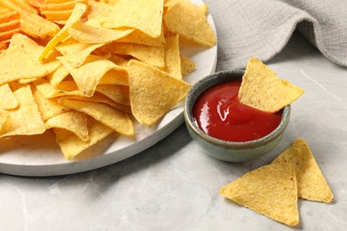 Photo of Tasty ketchup with ridged and tortilla chips on grey table