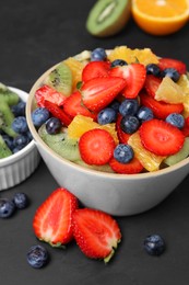 Photo of Delicious fresh fruit salad in bowl and ingredients on dark table