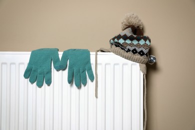 Photo of Modern radiator with knitted hat and gloves near beige wall indoors