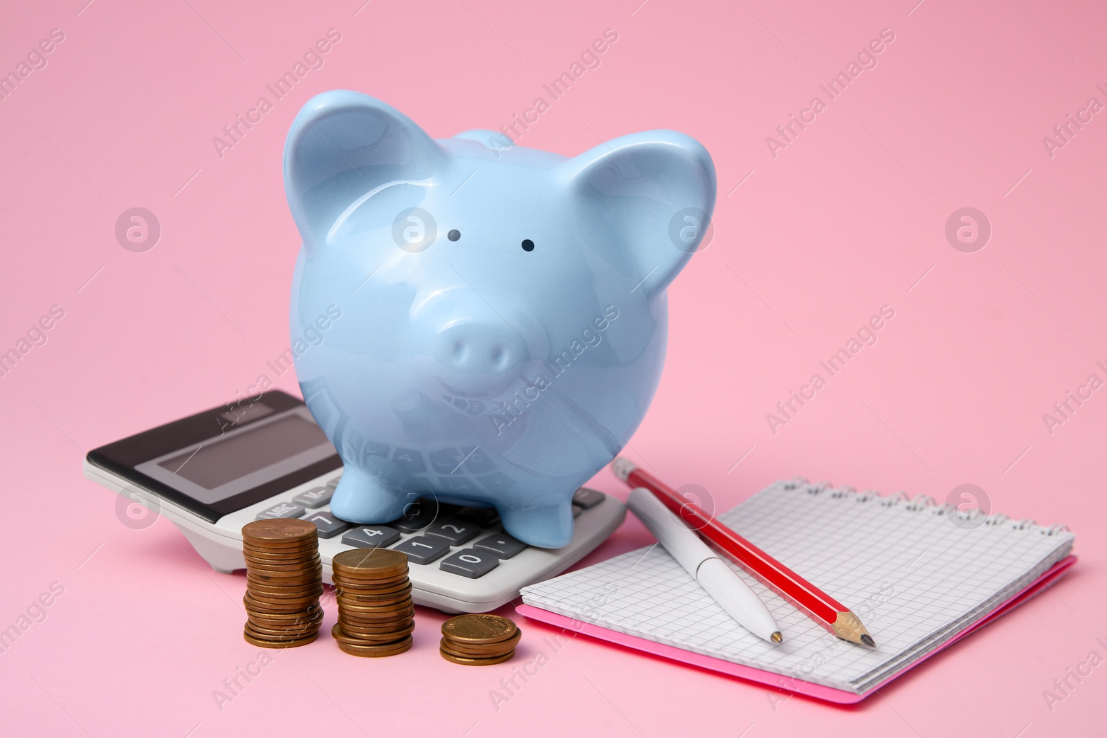 Photo of Piggy bank, coins and stationery on pink background