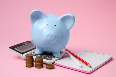 Photo of Piggy bank, coins and stationery on pink background