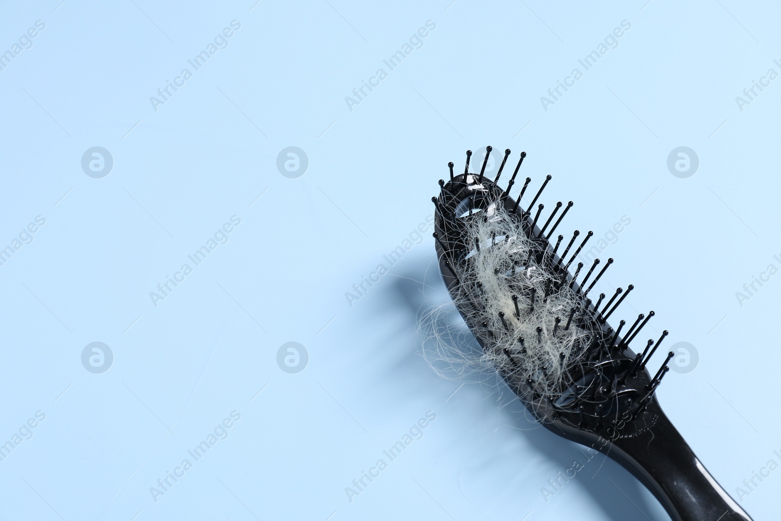 Photo of Brush with lost hair on light blue background, space for text