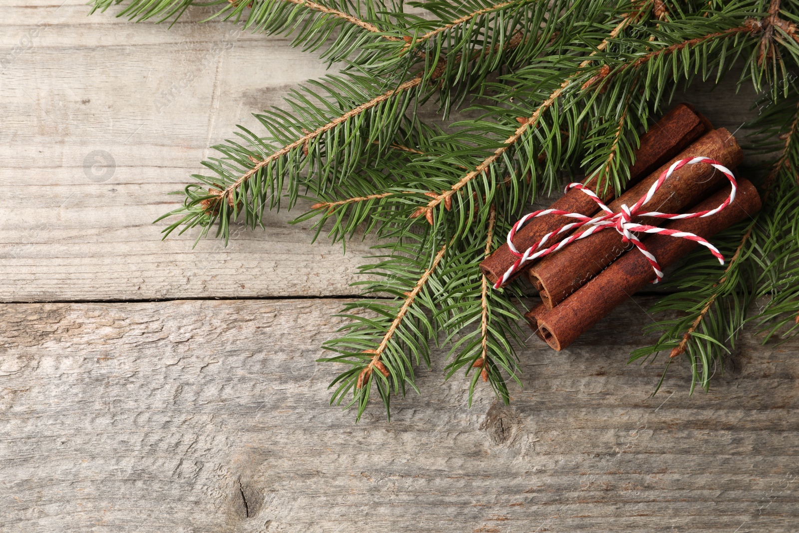 Photo of Cinnamon sticks and fir branches on wooden table, flat lay. Space for text