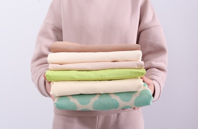 Woman holding stack of clean bed linens on light background, closeup