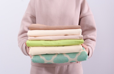 Photo of Woman holding stack of clean bed linens on light background, closeup