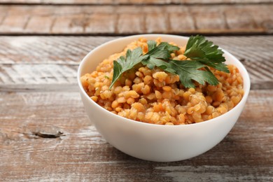 Delicious red lentils with parsley in bowl on wooden table, closeup. Space for text