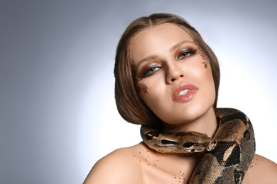Photo of Beautiful woman with boa constrictor on light grey background. Space for text