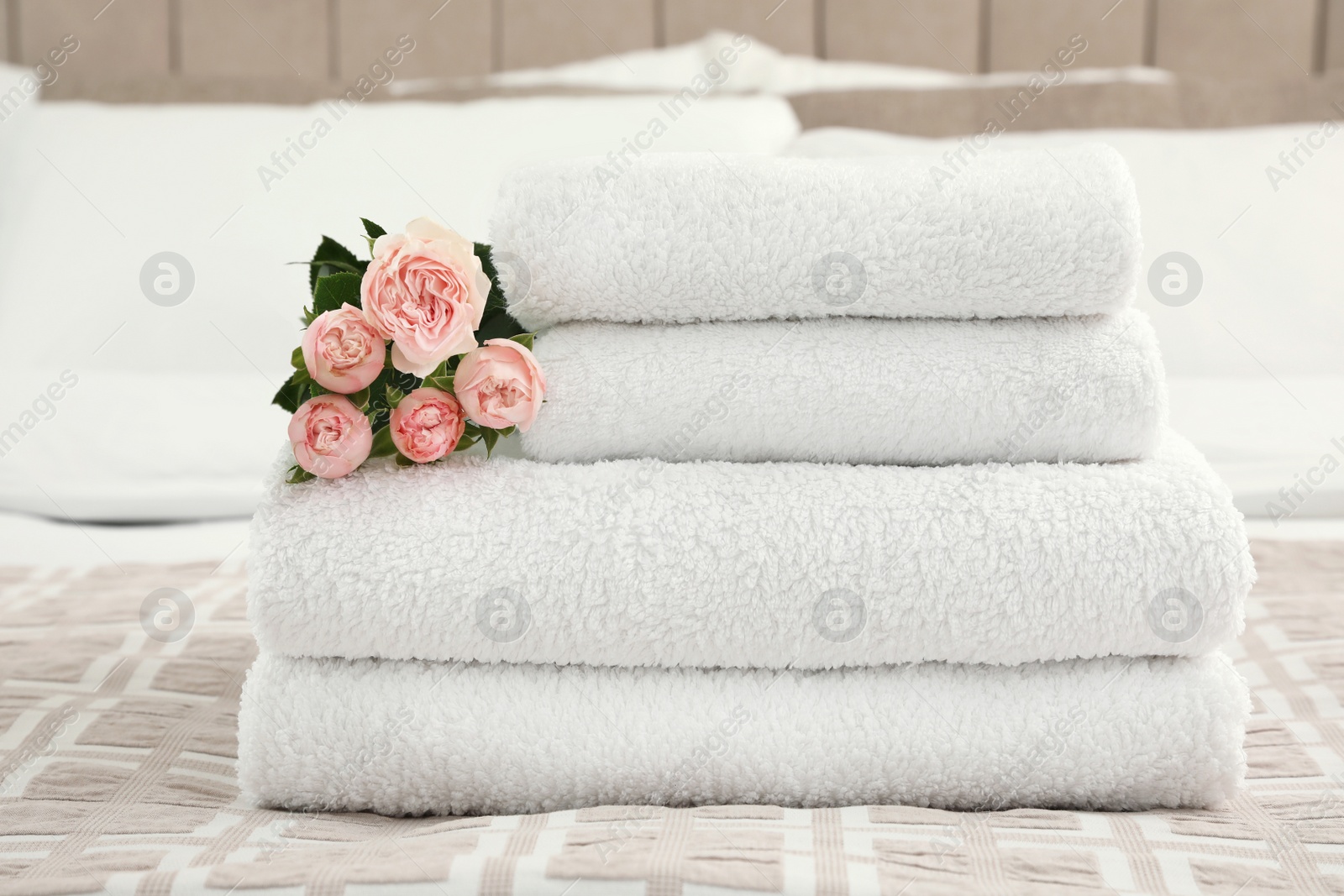 Photo of Stack of fresh towels with flowers on bed indoors