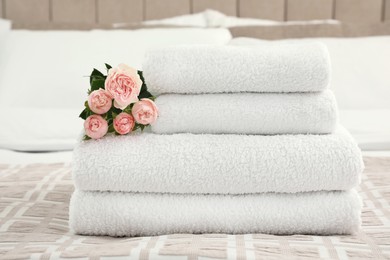 Stack of fresh towels with flowers on bed indoors