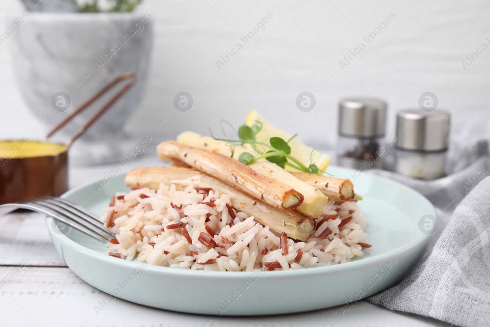 Photo of Plate with baked salsify roots, lemon, rice and fork on white wooden table