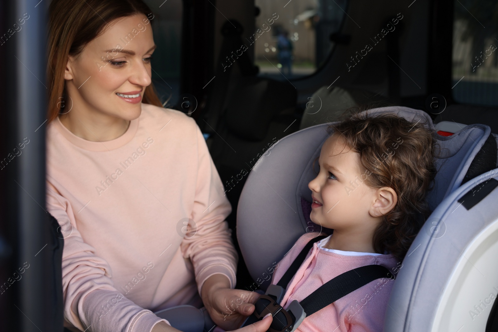 Photo of Mother fastening her daughter in child safety seat inside car