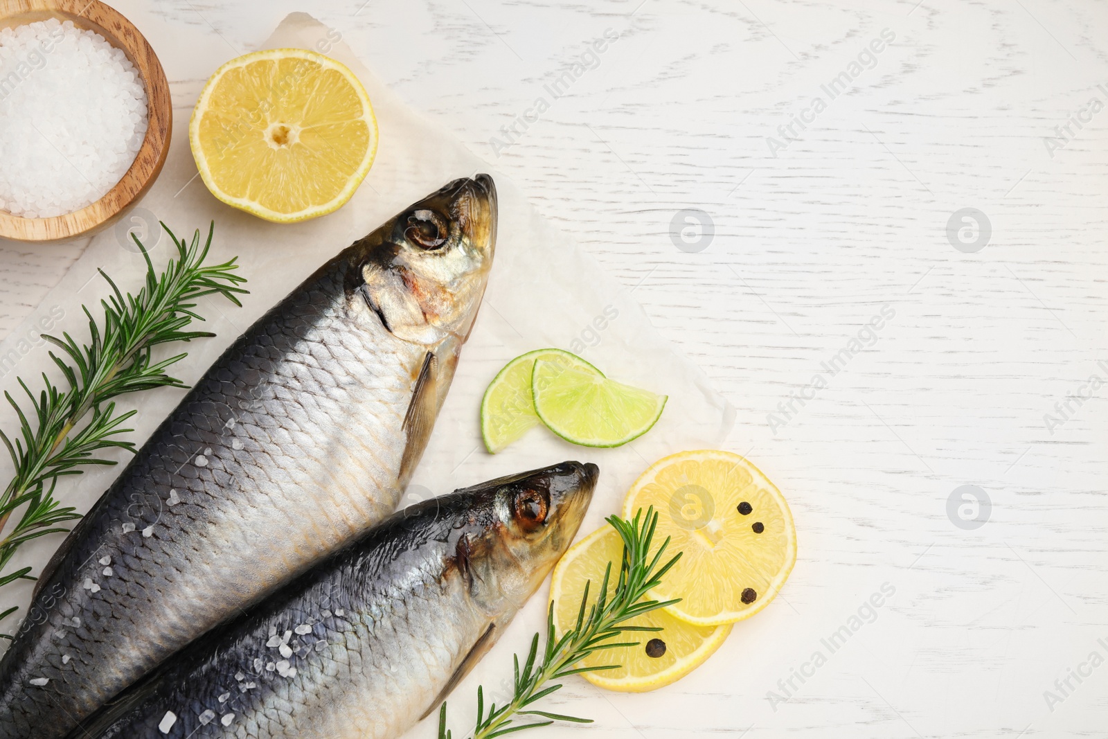 Photo of Delicious salted herrings, rosemary, salt and lemon on white wooden table, flat lay. Space for text