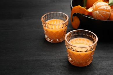 Photo of Tasty tangerine liqueur in glasses and fresh fruits on black wooden table. Space for text
