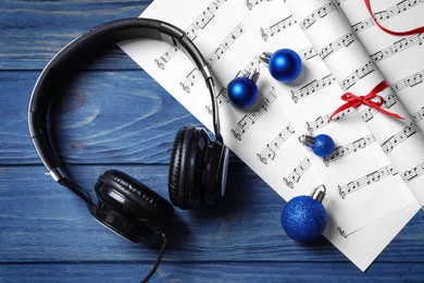 Photo of Flat lay composition with Christmas decorations, headphones and music sheets on blue wooden table