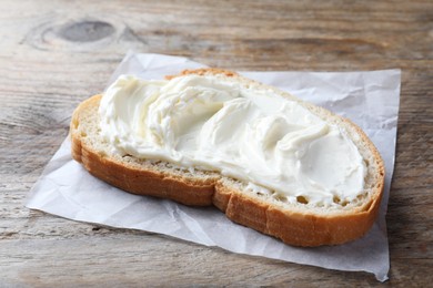 Photo of Slice of bread with tasty cream cheese on wooden table, closeup