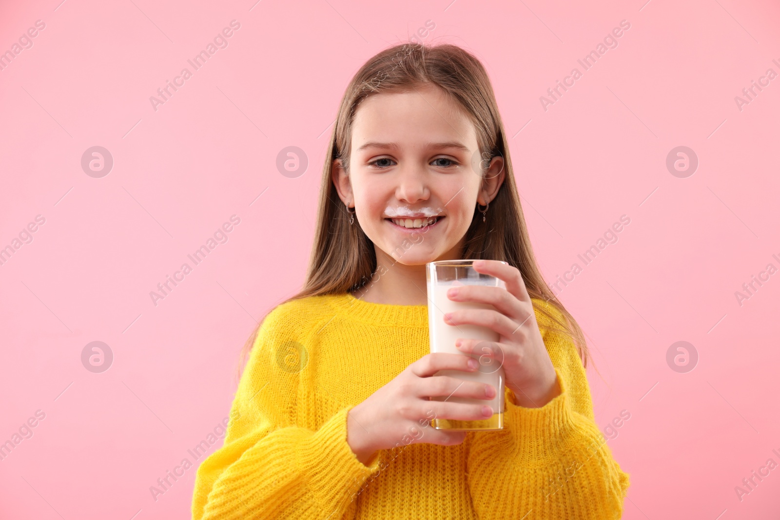 Photo of Happy little girl with milk mustache holding glass of tasty dairy drink on pink background