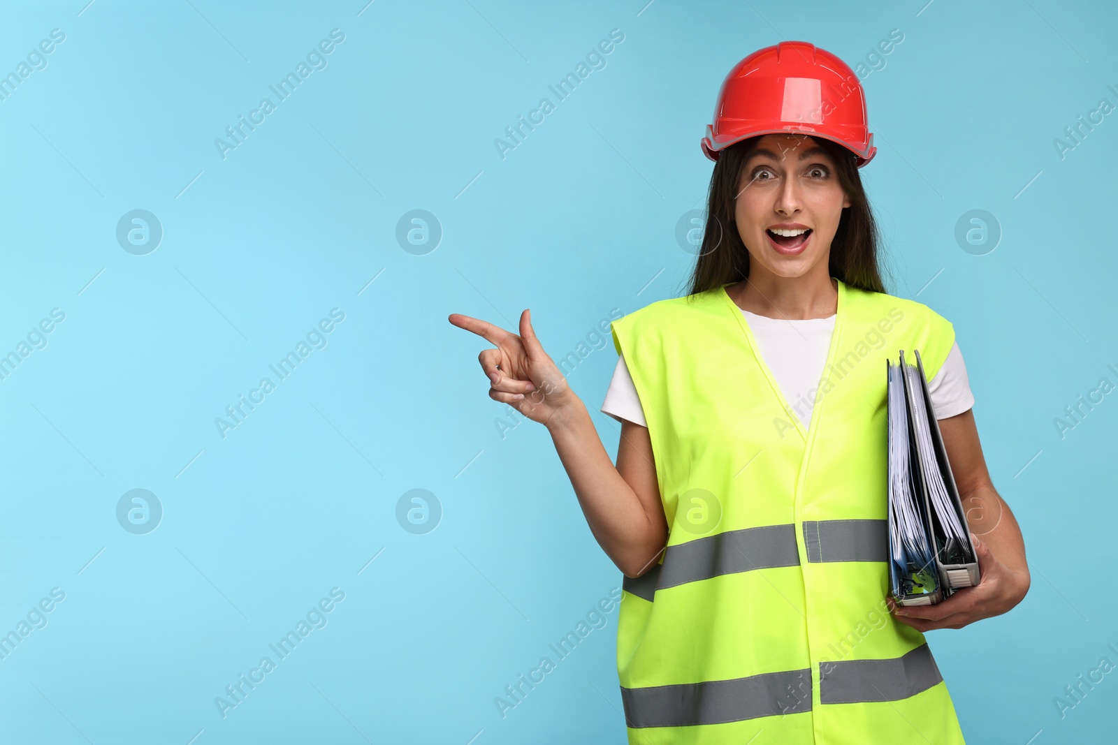 Photo of Architect in hard hat with folders pointing at something on light blue background, space for text