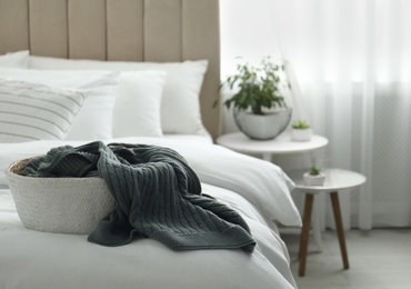 Basket with warm knitted plaid on bed indoors