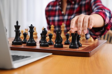 Photo of Woman playing chess with partner through online video chat at table indoors, closeup