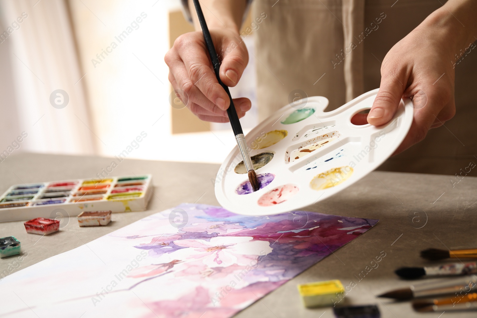 Photo of Woman painting flowers with watercolor at grey stone table in workshop, closeup