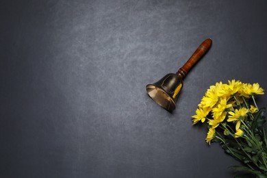 Photo of Golden school bell and bouquet of beautiful chrysanthemum flowers on blackboard, flat lay. Space for text