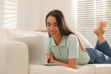 Photo of Young woman using laptop for search on sofa at home