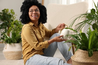 Photo of Happy woman watering beautiful houseplants at home