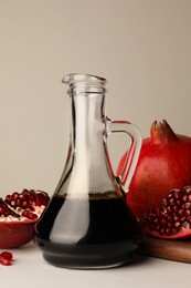Photo of Glass jug of tasty pomegranate sauce and fresh ripe fruits on white marble table